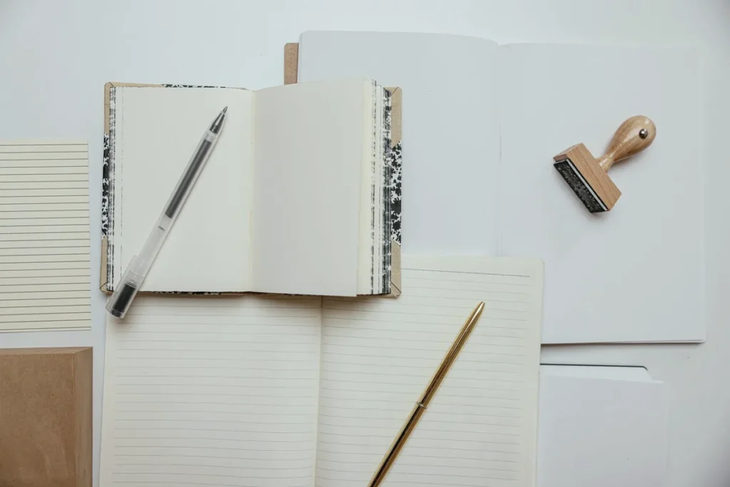 Aufgeschlagenes Notizbuch mit Stift und kleinem Holzstempel auf hellem Untergrund