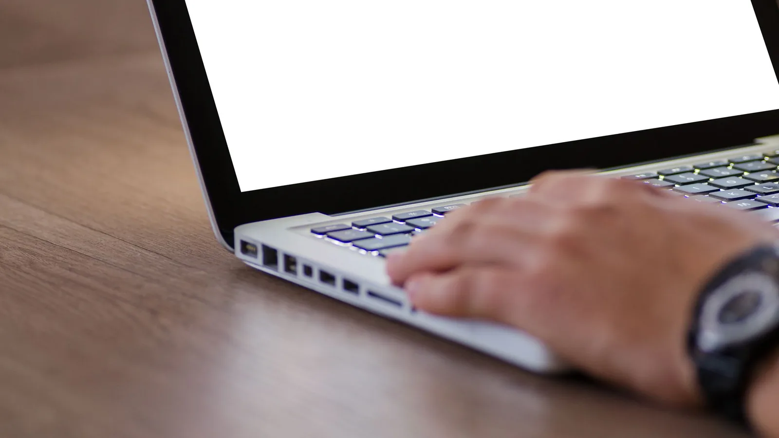 Hand auf der Tastatur eines Laptops mit weißem Bildschirm auf einem Holztisch